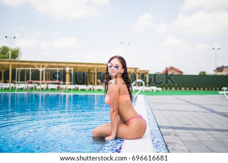Beautiful young woman sitting by swimming-pool. Summer.