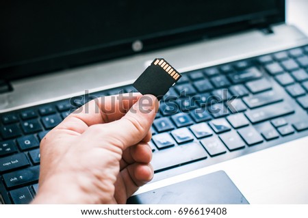 Photographer is holding  the flash drive with a laptop background in the office.