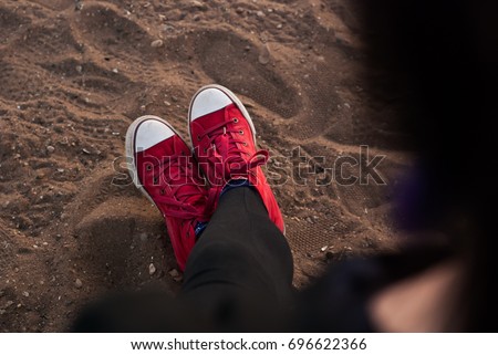 Woman legs in red shoes on the sand, relaxing on the beach