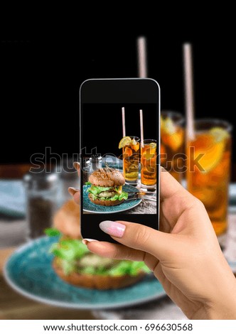 Photographing food concept - woman takes picture of sandwich with chicken burger, cheese and lettuce