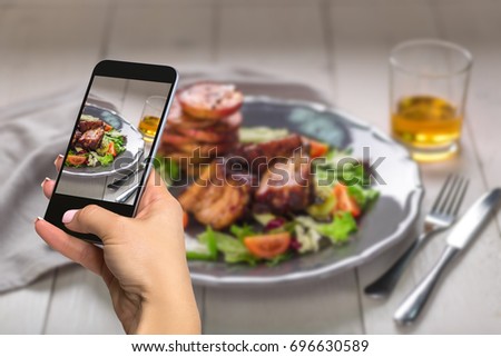 Photographing food concept - woman takes picture of hot meat dishes. Pork ribs grilled with salad and apples on a plate.