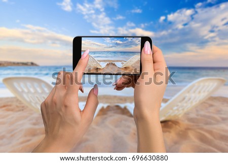 Photographing travel concept - woman takes picture of two beach chairs on the sand near sea and colorful sky
