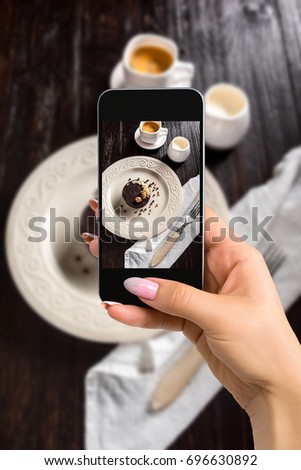 Photographing food concept - woman takes picture of beautiful decorated chocolate cake with golden nuts and a cup of coffee