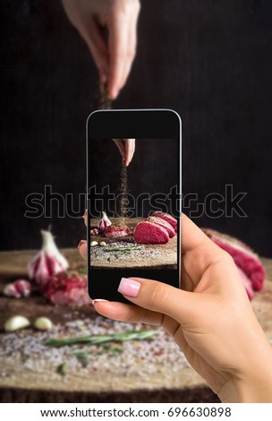 Photographing food concept - woman takes picture of juicy raw beef steak on wooden table