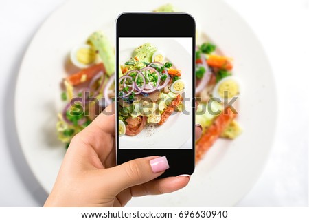 Photographing food concept - woman takes picture of fresh salad with lettuce, eggs, tomatoes, onion rings, peppers
