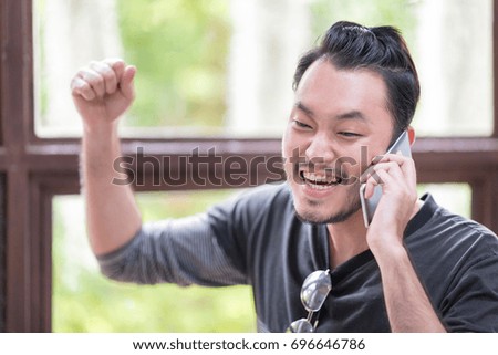 Happy Asian man winning something while talking on smartphone in the Vintage wooden coffee shop cafe.