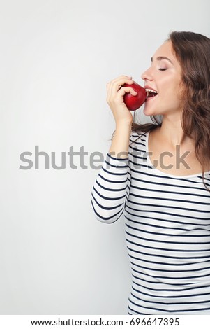 Portrait of young woman with apple on grey background