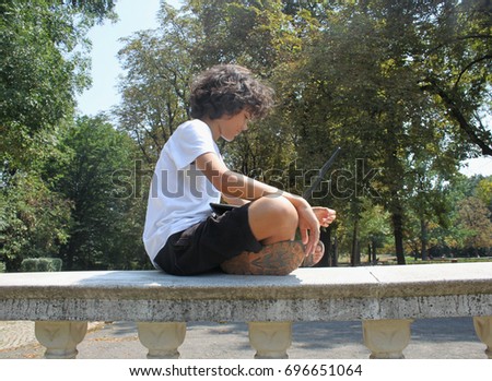 A handsome curly boy is sitting in the park with a laptop on his legs, expressions