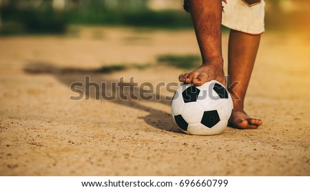 An action picture of an old ball and foot of a kid who is playing football in the sunshine day for exercise.Low key style.