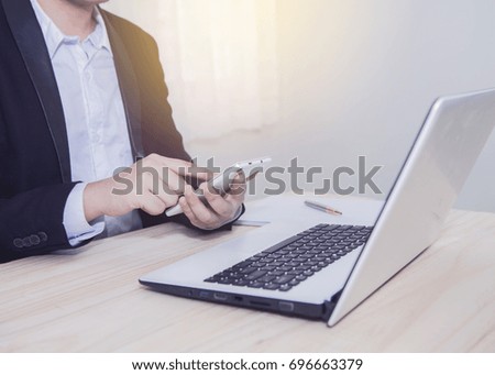 businessman using smart phone in front of laptop on wooden table in office