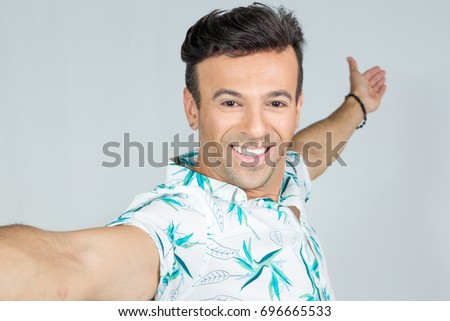 Man smiles and takes a picture. Selfie. He is handsome and hands point in one direction. POV. Personal perspective. Point of view. Brazilian man wearing a floral shirt, Hawaiian style. Summer