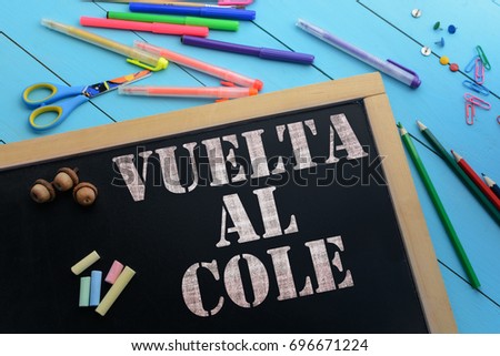 The text Back to school (Spanish language) on black chalkboard on the table with school accessories (pens, pencils, brushes)