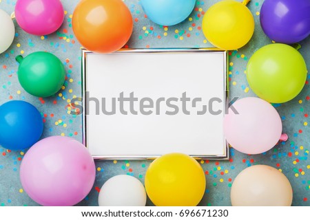 Colorful balloons, silver frame and confetti on blue background top view. Birthday or party mockup for planning. Flat lay style. Copy space for text. Festive greeting card.