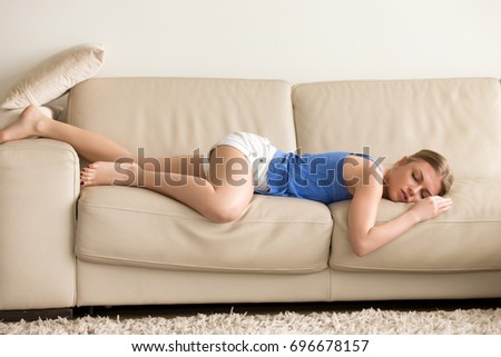 Tired funny young woman in summer everyday clothes stretches out and sleeps on sofa at home. Female student asleep in morning in living room after party, taking break for short sleep in middle of day Royalty-Free Stock Photo #696678157
