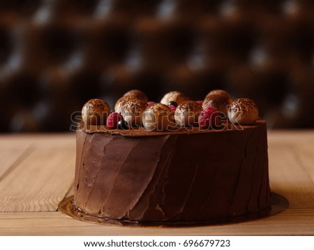 Close-up of a chocolate cake with raspberries and black currants a confectioner puts on a table on blurred background.