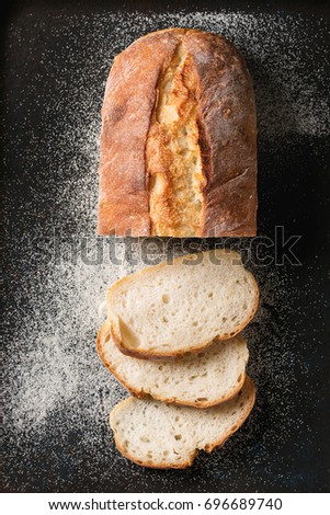 Sliced homemade white wheat bread with wheat flour on old black oven tray as background. Top view Royalty-Free Stock Photo #696689740