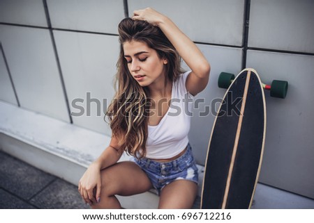 Young woman is posing with skateboard in the city. Female teenager outdoor with long board.