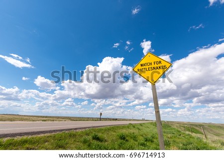 Bright yellow caution sign on side of road warning drivers to watch for rattlesnakes on the highway
