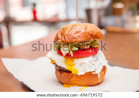 Fresh Tasty Beef Burger with lettuce, tomato, bacon, cheese and fried egg on a paper tray ready be take away on the bar counter. Selective focus, close up. Fast food cafe cuisine. Space for text