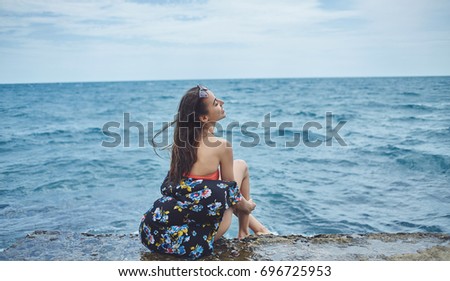 Young laughing girl wearing in bikini sits on background of sea