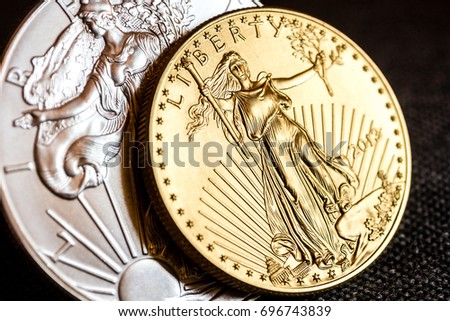 closeup of silver eagle and golden american eagle one ounce coins on black background