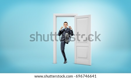 A young businessman stands in a small cut out doorframe and kicks a door open with his foot. Self-made executive. Fight bureaucracy. Get things done. Royalty-Free Stock Photo #696746641