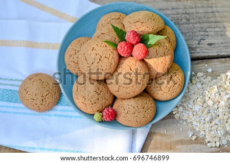 Oatmeal cookies in a bowl and raspberry next towel oatmeal scattered beside