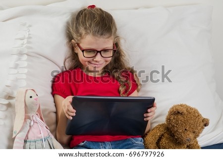 Pretty girl with glasses watching cartoon, video on her tablet and smiling. Rest at home.