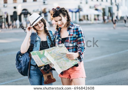 Two beautiful tourist girls with a map walk around the old city
