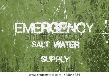 Old and worn white lettering 'Emergency Salt Water' sign on chipped green painted background texture.