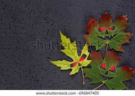 Halloween decor - autumn maple leaves with evil faces and red eyes. Black background. Copy Space