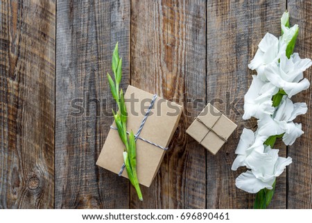 Gift box wrapped in craft paper near flower gladiolus on wooden background top view copyspace
