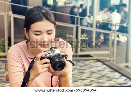 pretty cool young Asian woman with retro film camera or mirrorless camera in modern garden open mall.young woman holding mirrorless camera in vintage tone