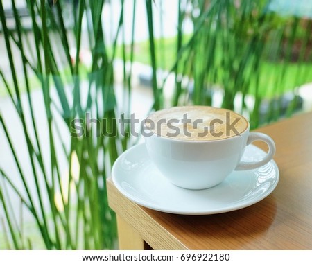 Hot coffee white glass white saucer brown table green tree backdrop