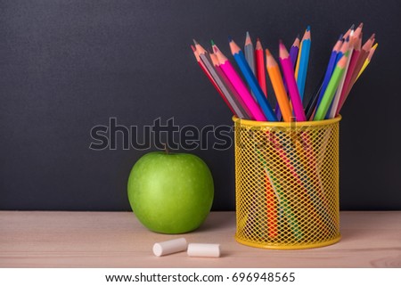 education concept with green apple, pencils, chalks over black chalkboard background, close up