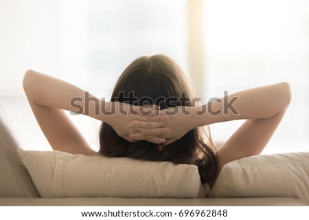 Relaxed woman resting on sofa hands behind head, breathing fresh air, enjoying peaceful moment, feeling no stress, relaxing on comfortable couch at home, practicing yoga and meditation, back view Royalty-Free Stock Photo #696962848