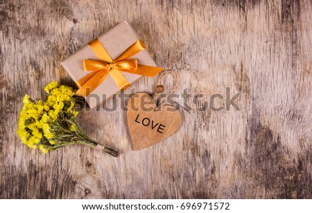 A box with a gold ribbon on an old wooden background. Wooden heart and flowers. Copy space. Flat lay