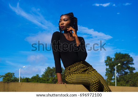 african girl sitting on fence with blue sky background and looking towards the sun