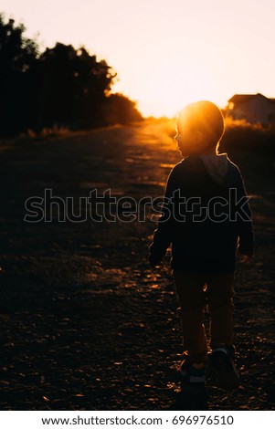 Blurred picture a little young boy silhouette walking on sunset lights with sun beaming into the camera