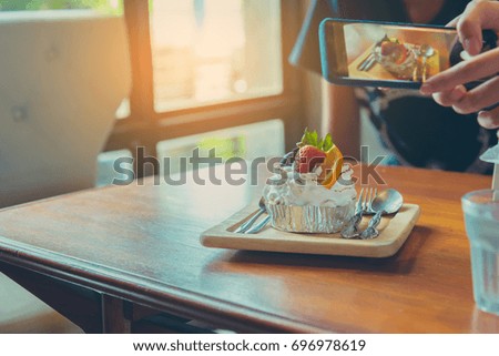 vintage tone image of mixed fruit Cake with blue berry strawberry and orange on wood table with hand hold smart phone to take photo of food.(focus on cake)