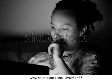 Young woman working on a laptop computer late at night; light from the monitor lights her face