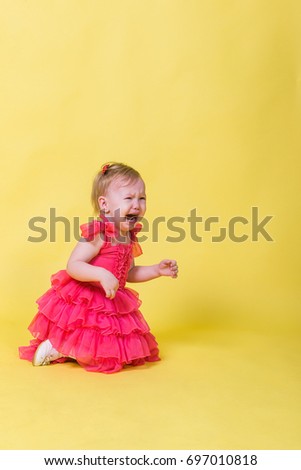 Little girl in pink dress kneeling and crying on a yellow background