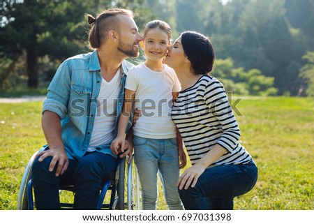 Lovely mother and father kissing their daughter on cheeks