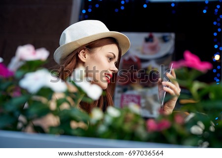 Beautiful young woman with a smile looking into the phone doing selfie, taking pictures of herself, flowers in the foreground on a summer veranda                               