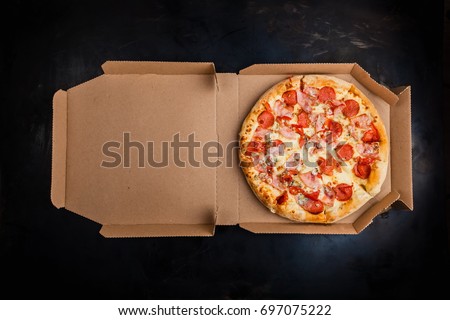 Pizza in a cardboard box against a dark background. Space for text. View from above. Pizza delivery. Pizza menu. Royalty-Free Stock Photo #697075222
