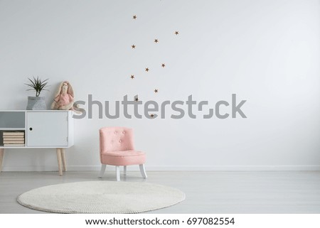 Scandi style girl's bedroom with a plant standing on a white cupboard next to a pink, chic chair, and a white circular carpet Royalty-Free Stock Photo #697082554