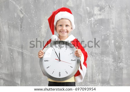 Cute little girl in Santa Claus suit with clock on grunge background. Christmas countdown concept