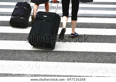 two persons with suitcase go over a crossway