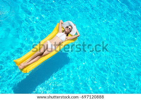 Beautiful young woman with inflatable mattress in blue swimming pool