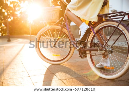 Cropped image of a young female in dress riding bicycle outdoors